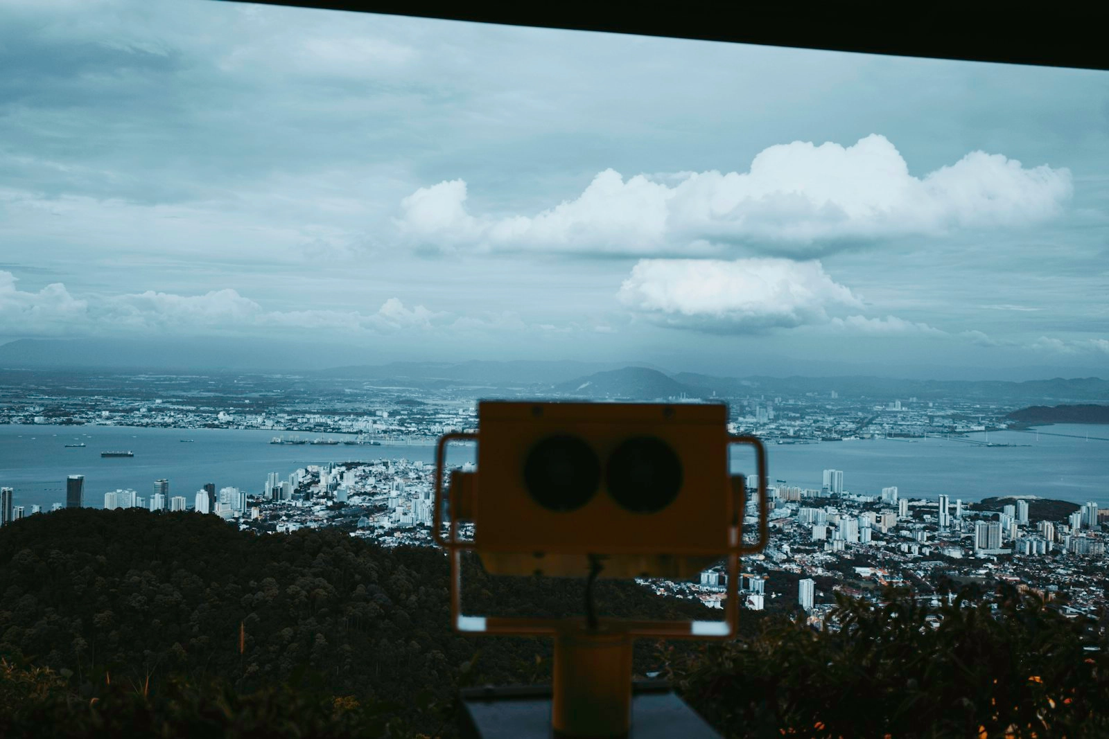 Binoculars overlook a coastal city under cloudy skies.